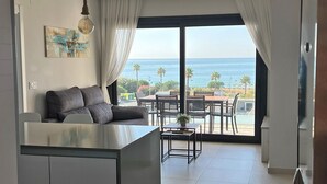 A modern kitchen with a central island, a dining area with a table and chairs, and a view of the ocean through large windows.