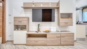 A modern living room with a built-in TV, wooden cabinets, and a small kitchen area. - Margaret House Sorrento (Sorrento)
