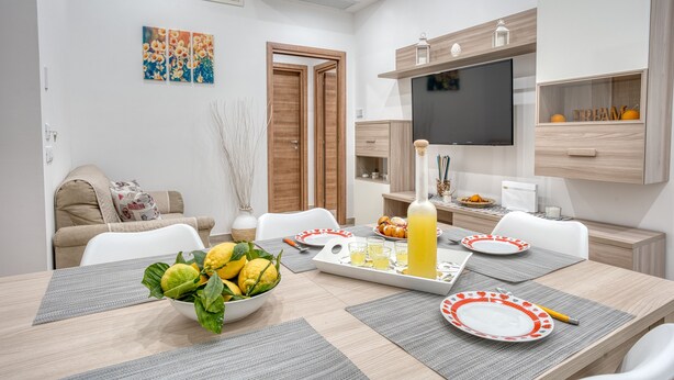 A modern dining area with a table set for four, a bowl of lemons, and a bottle of juice. - Margaret House Sorrento (Sorrento)