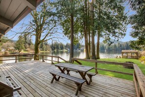 A wooden deck with picnic tables overlooking a lake, surrounded by trees and a gazebo. - Thompson Cabin- Lake Front (Sedro-Woolley)