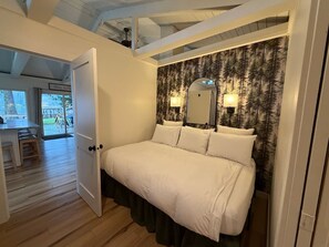 A bedroom with a bed, a mirror, and a wall with a forest pattern. - Thompson Cabin- Lake Front (Sedro-Woolley)