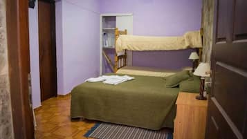 Una habitación con una cama litera, una mesita de noche con lámpara, un pequeño estante y una puerta.