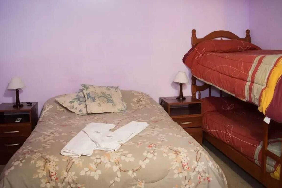 A bedroom with a single bed, a wooden headboard, two bedside tables with lamps, and a bunk bed.