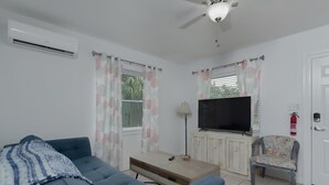 Ett vardagsrum med en blå soffa, en tv, en takfläkt och ett fönster med gardiner.