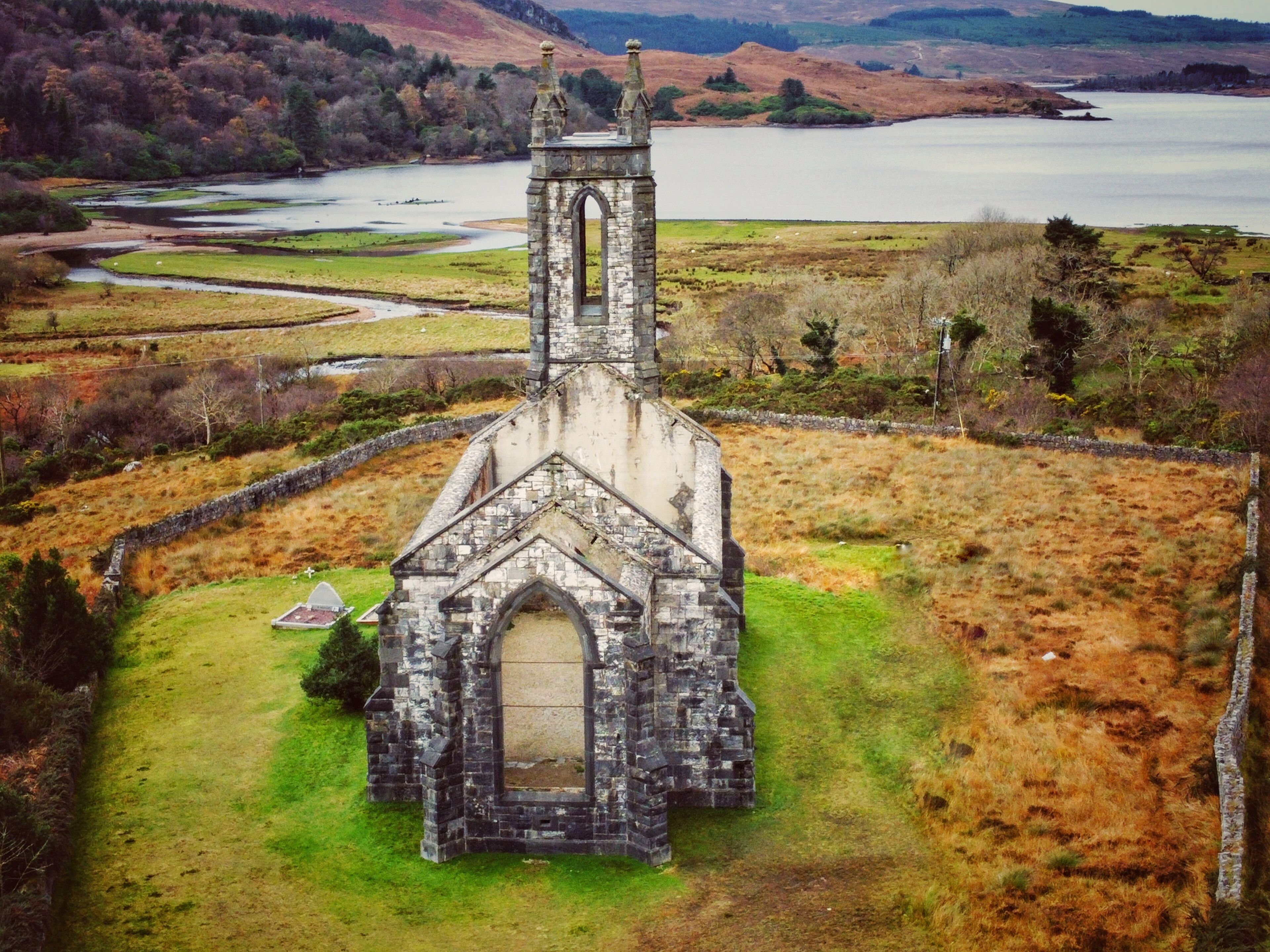 Une vieille église en pierre, dotée d’un clocher, entourée d’une pelouse et avec une étendue d’eau en arrière-plan.