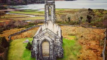 Une vieille église en pierre, dotée d’un clocher, entourée d’une pelouse et avec une étendue d’eau en arrière-plan.