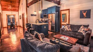 A cozy living room with a sofa, coffee table, and a kitchen area with blue cabinets and a refrigerator. - Romantic Couples Cabin minutes from Casino Excitement & Lakeside Serenity (Broken Bow)