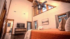 A bedroom with a large bed, a ceiling fan, a TV, and a window with curtains. - Romantic Couples Cabin minutes from Casino Excitement & Lakeside Serenity (Broken Bow)