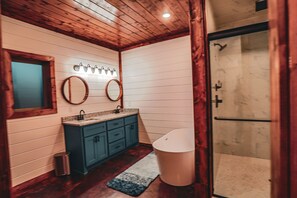 Un bagno con soffitto in legno, pareti bianche, un lavabo con specchio e una zona doccia.