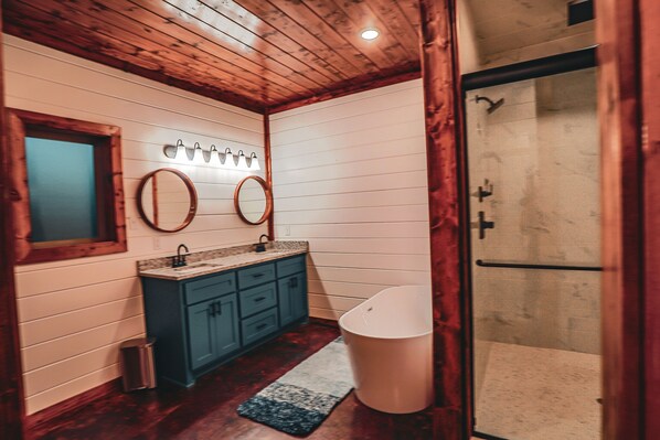 Un baño con techo de madera, paredes blancas, un lavabo con espejo y zona de ducha.