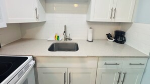 Eine Küche mit weißen Schränken, einer Edelstahlspüle, einer Kaffeemaschine und einem Papierhandtuchhalter.