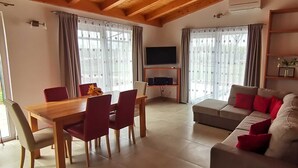 Un salon moderne avec une table à manger en bois, des chaises rouges, un canapé gris avec des coussins rouges et un téléviseur à écran plat posé sur un meuble en bois.