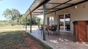 Un espace extérieur aménagé en patio, avec un coin salon abrité, une table en bois et des chaises.