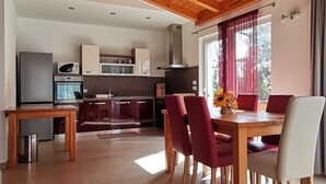 Une cuisine moderne dotée d’appareils électroménagers intégrés, un coin repas avec des chaises rouges et une grande fenêtre agrémentée de rideaux.