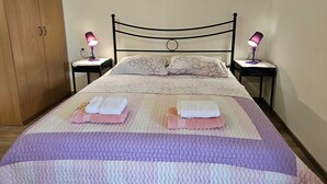 Een net opgemaakt bed met een beddengoed met een patroon en twee kussens, zijkanten omlijst door twee nachtkastjes met lampen.