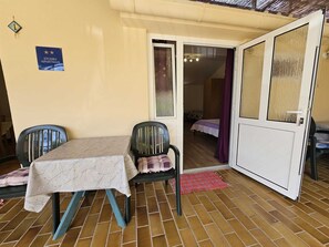 Un monolocale con pavimento piastrellato, un tavolo con tovaglia floreale, due sedie, un letto con tenda viola e un cartello che indica che si tratta di un monolocale.