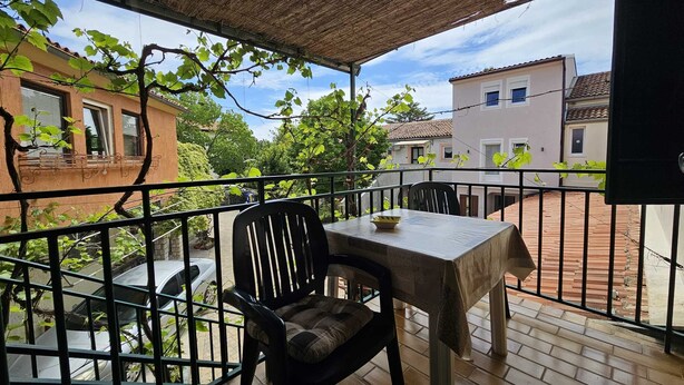 A balcony with a table and chairs, a thatched roof, and a view of neighboring buildings. - La Pergola - Yellow - Studio Apartment (Rovinj)