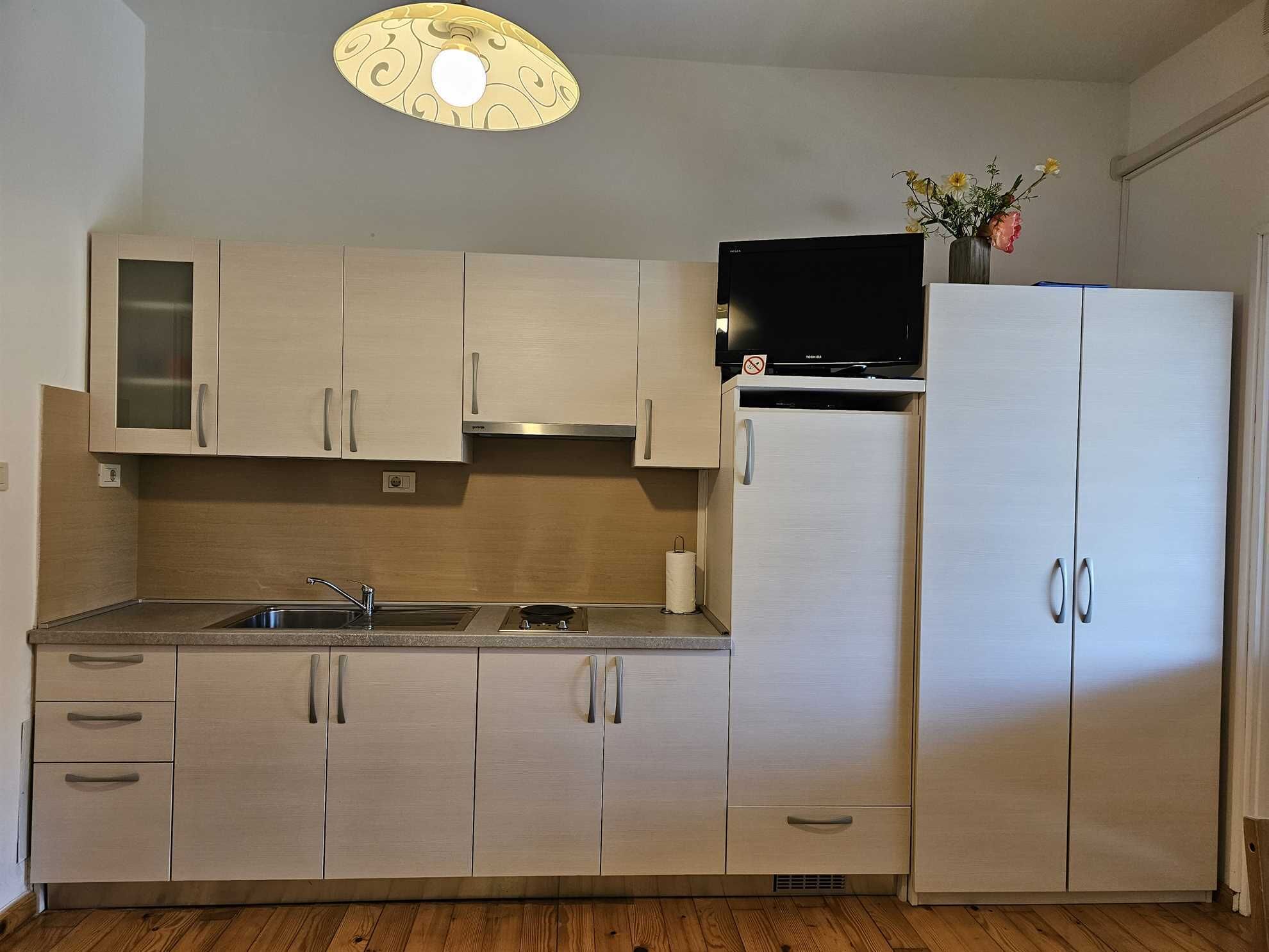A compact kitchen with light wood cabinets, a stainless steel sink, a built-in stove, and a refrigerator.