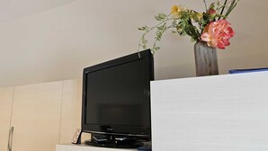 A flat-screen TV on a wooden cabinet, a vase with flowers, and a blue pen on a white surface. - La Pergola - Yellow - Studio Apartment (Rovinj)