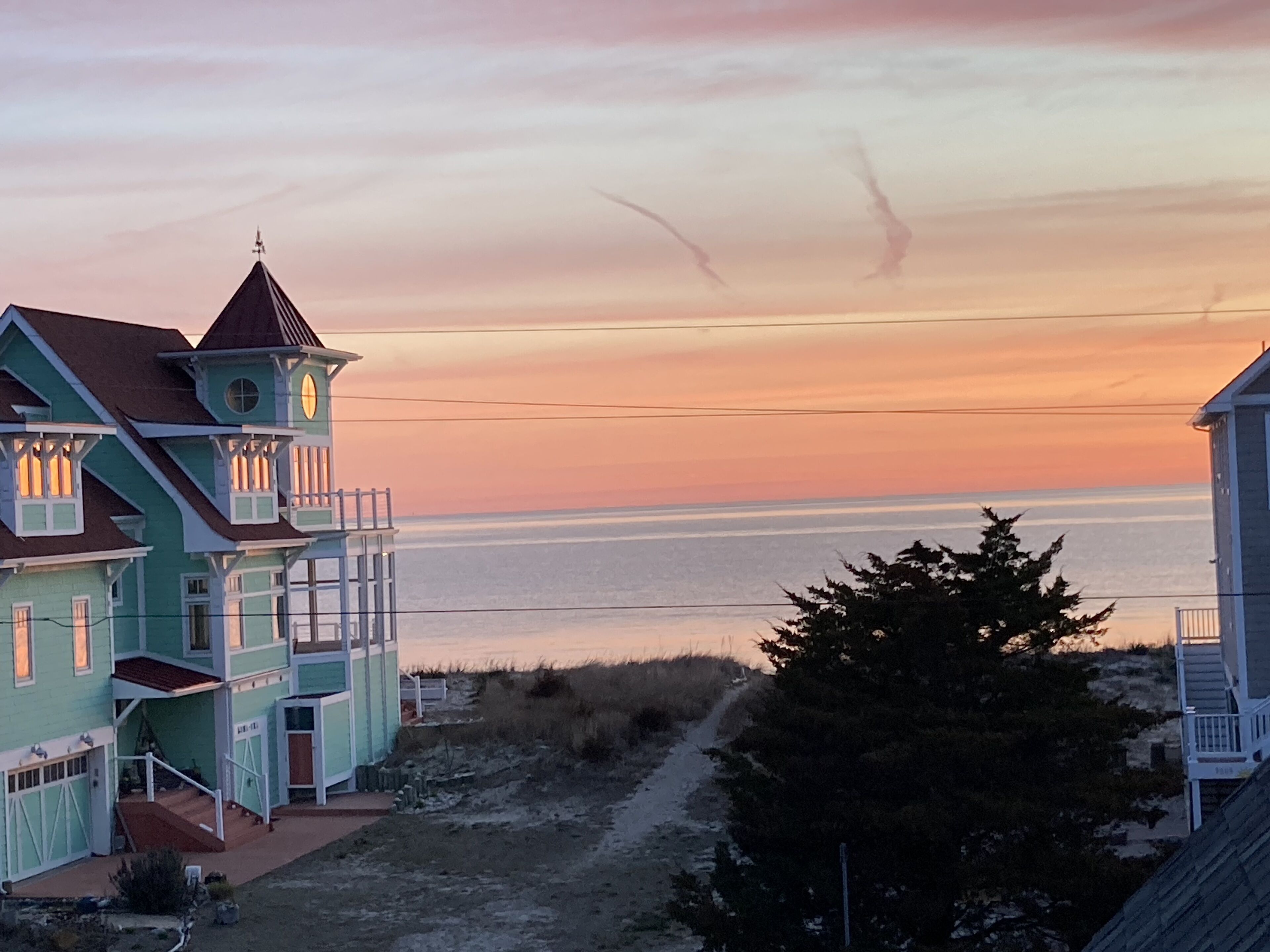 A coastal house with a balcony overlooking the sea, a path leading to the entrance, and a nearby tree.