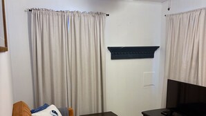 Een woonkamer met een bruine bank, een klein zwart tafeltje, een tv-meubel, een plafondventilator en een kamerbreed tapijt met dessin.