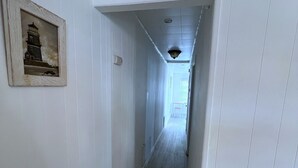 A narrow hallway with white walls and wooden flooring, leading to a door at the end. - BEACH HOUSE - half block from beach (Belmar)
