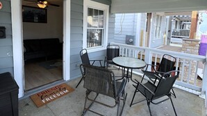 Een overdekt terras met een plafondventilator, een ronde tafel en vier stoelen.