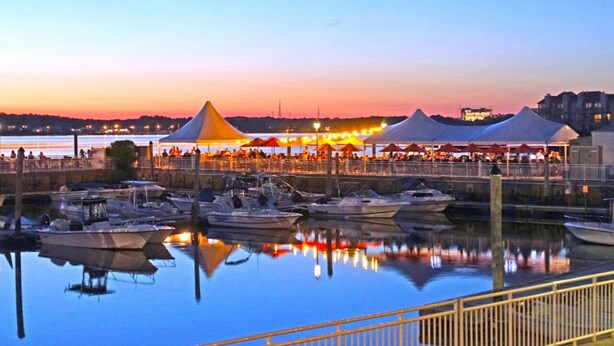 Een jachthaven met aangemeerde boten, tenten voor een evenement en uitzicht op het water.