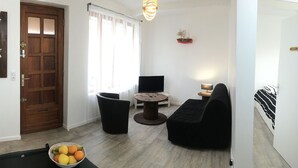Ein Wohnzimmer mit Holztür, Fernseher, rundem Couchtisch und schwarzem Sofa.