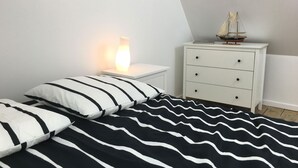 Ein Schlafzimmer mit einem Bett, einem Nachttisch mit Lampe, einer Kommode und einem Modellschiff.