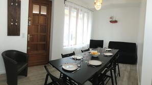 Ein Essbereich mit Holztisch, gedeckten Plätzen für vier Personen, schwarzen Stühlen, einem Fenster mit durchsichtigen Vorhängen, einer Holztür und einer kleinen Schiffdekoration an der Wand.
