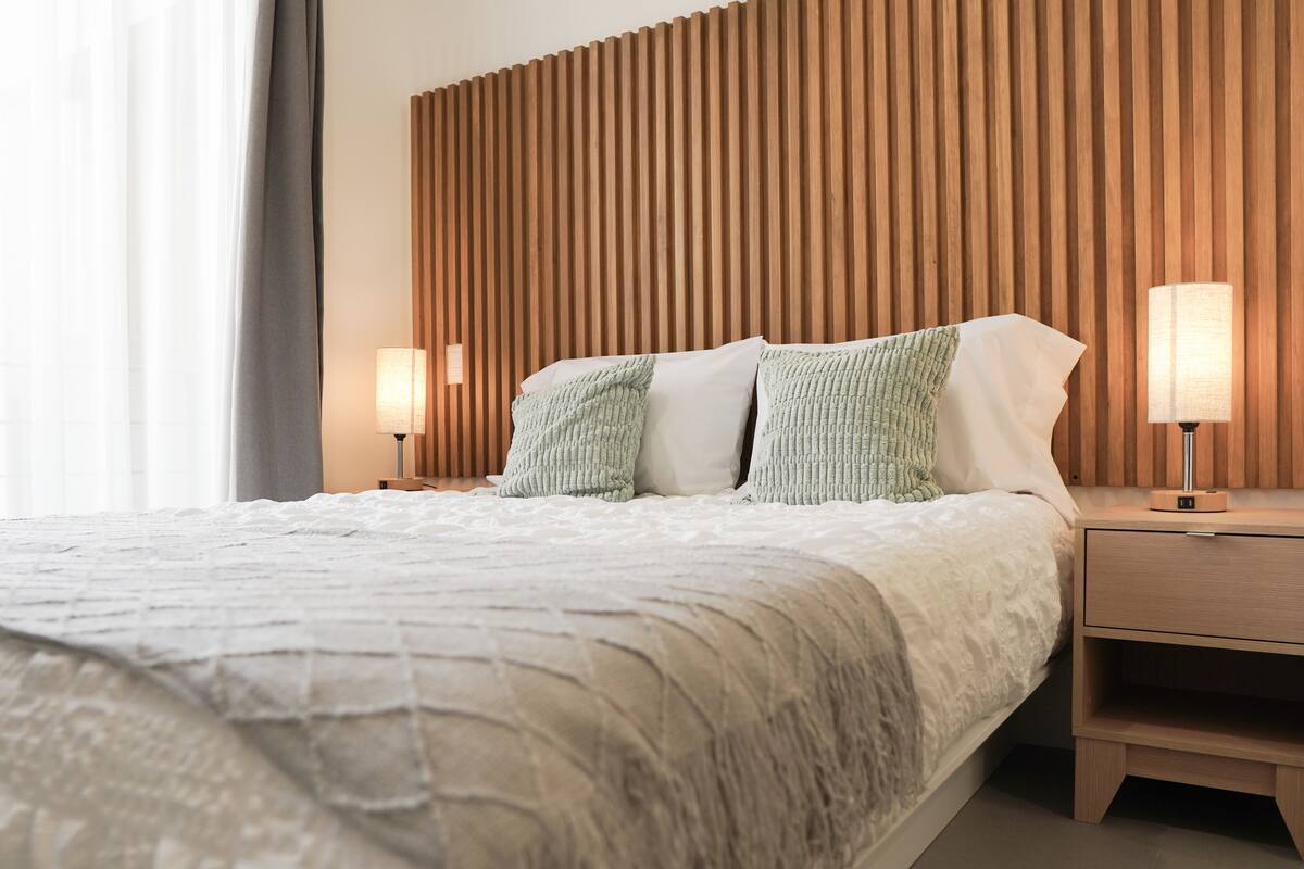 A neatly made bed with a white duvet and two pillows, flanked by wooden nightstands with lamps.