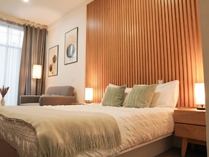 A hotel room with a large bed, a sitting area with a chair, and a wooden panel wall.