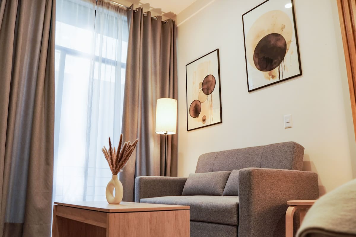A modern living room with a grey sofa, a wooden coffee table, and a lamp. There are two framed artworks on the wall.