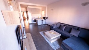 A modern living room with a grey sofa, a wooden coffee table, and a kitchen in the background.