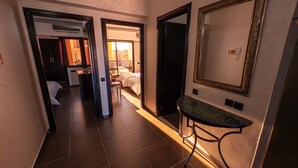 A hotel hallway with a bed, a bathroom, and a sitting area with a table and chair.