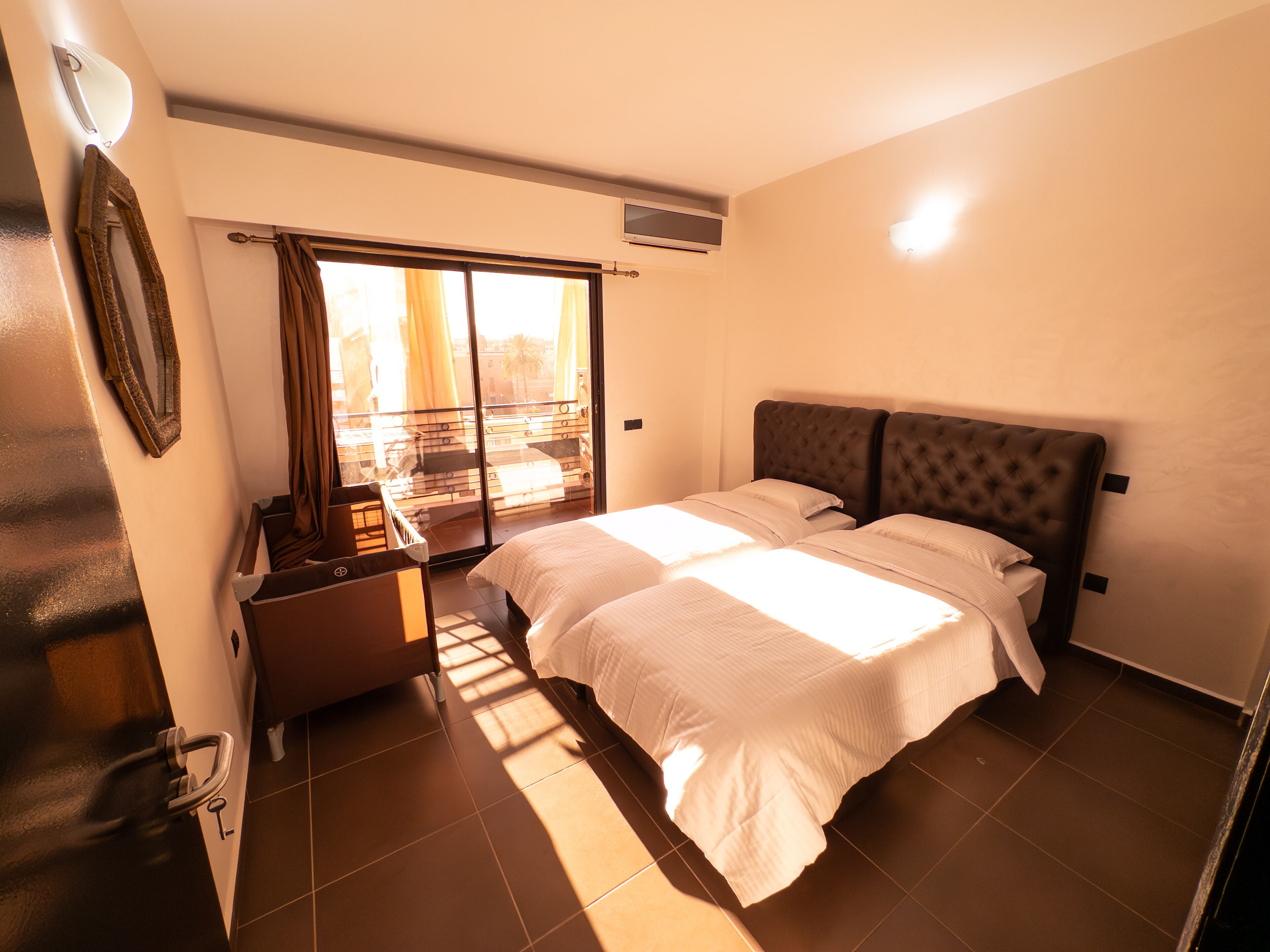 A bedroom with a large bed, a small table, a mirror, and a sliding door to a balcony.