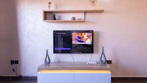 A modern living room with a flat-screen TV mounted on a wall, a wooden entertainment unit below, and a small shelf with decorative items.