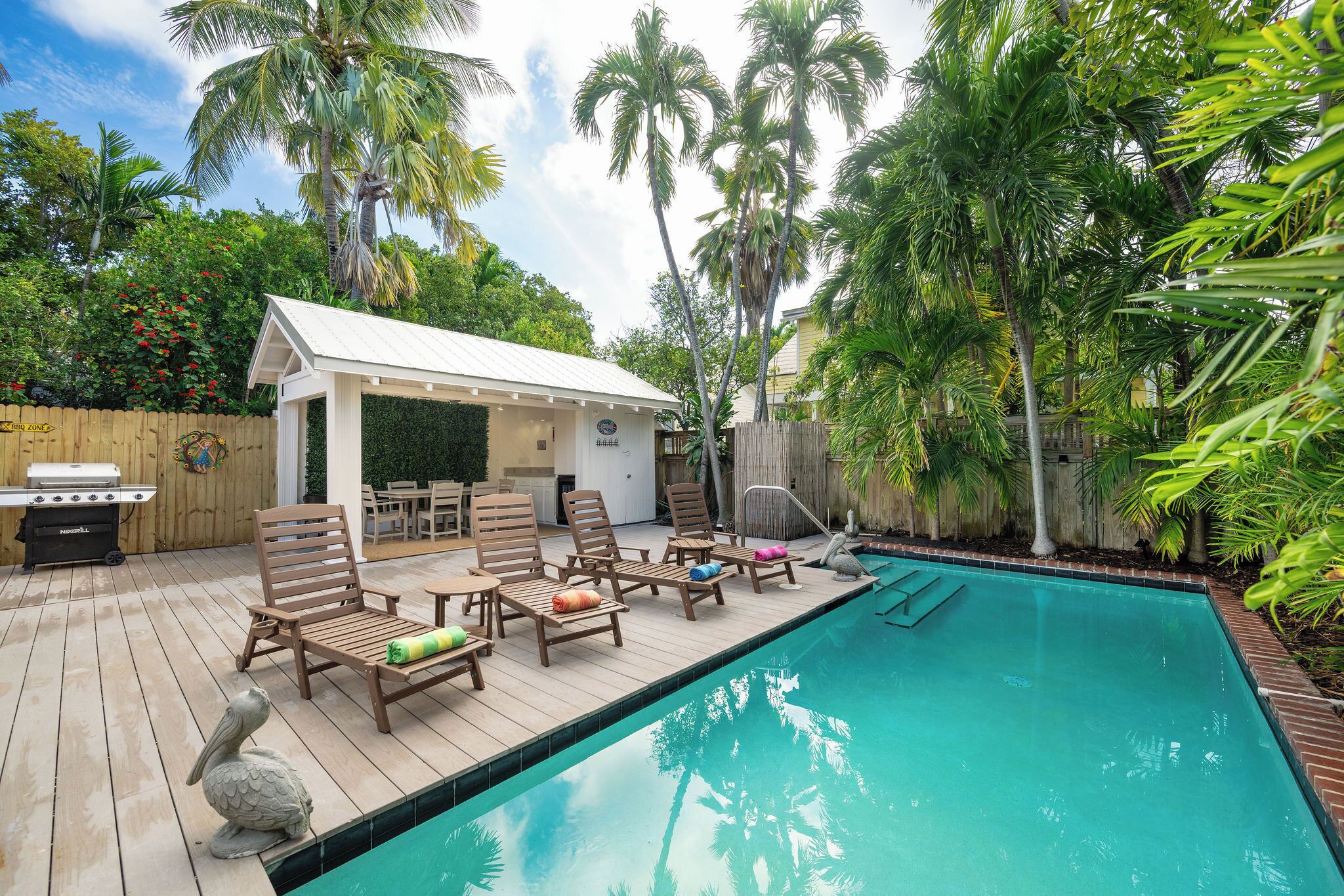 A poolside area with wooden deck, lounge chairs, a barbecue grill, and a covered seating area.