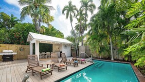 A poolside area with wooden deck, lounge chairs, a barbecue grill, and a covered seating area.