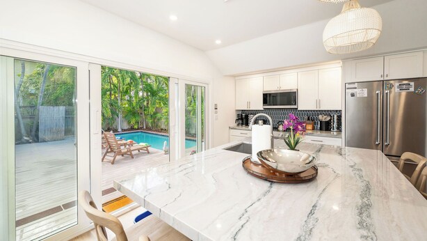 A modern kitchen with a large island, stainless steel appliances, and a view of a backyard with a pool.