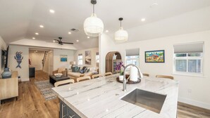 A spacious kitchen with a large island, modern pendant lights, and a view of the living area.