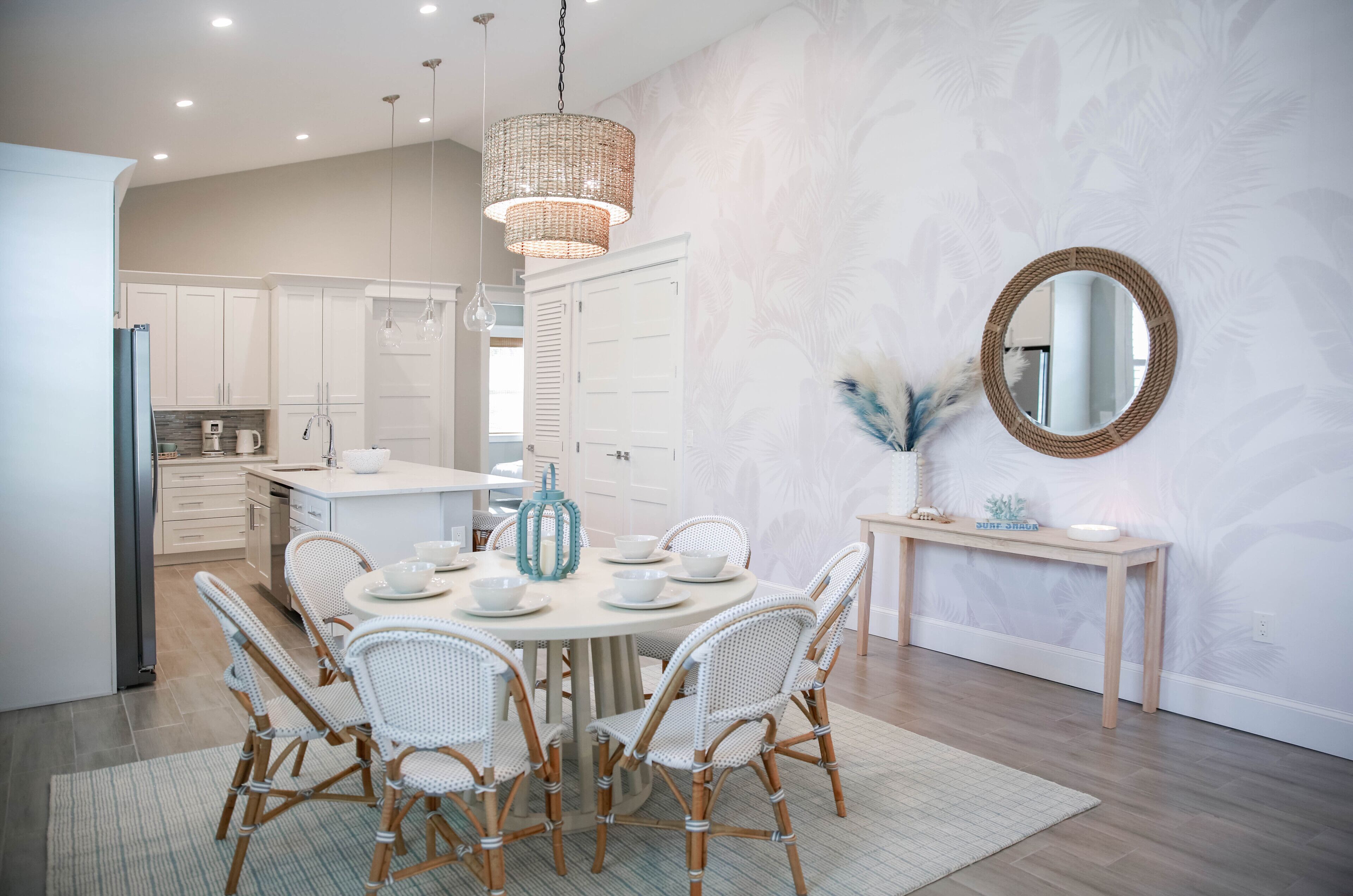 A modern kitchen with white cabinetry, a dining area with wicker chairs, and a round mirror on the wall.