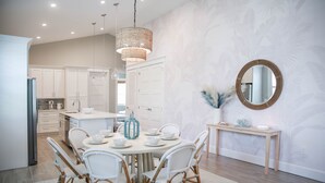 Une cuisine moderne avec des meubles blancs, un coin repas doté de chaises en osier et un grand miroir rond accroché au mur.