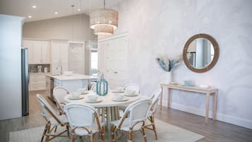 A modern kitchen with white cabinetry, a dining area with wicker chairs, and a round mirror on the wall.
