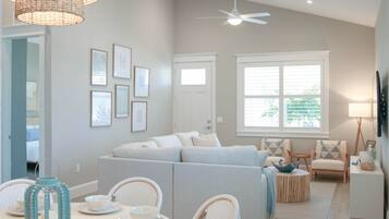 A modern living room with a white sofa, a dining table with chairs, and a ceiling fan.