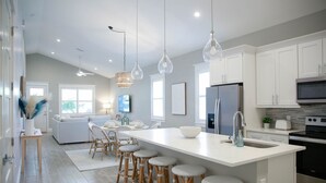 Une cuisine moderne avec des meubles blancs, un grand îlot central doté de tabourets, un réfrigérateur et un four à micro-ondes.