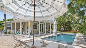 A pool area with lounge chairs, a covered patio, and a pool.