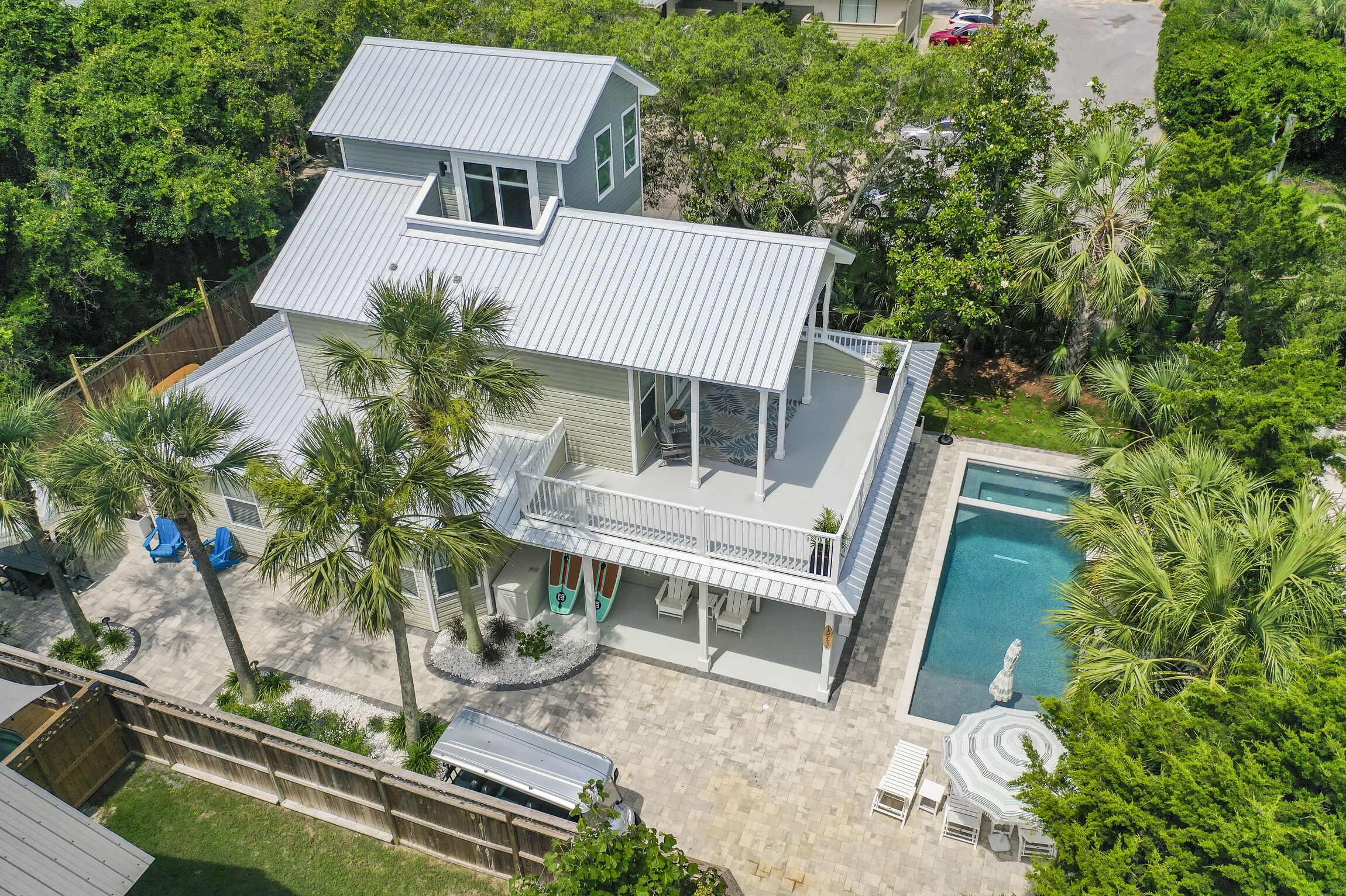 A two-story house with a swimming pool, surrounded by palm trees and a fenced yard.
