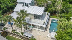 A two-story house with a swimming pool, surrounded by palm trees and a fenced yard.